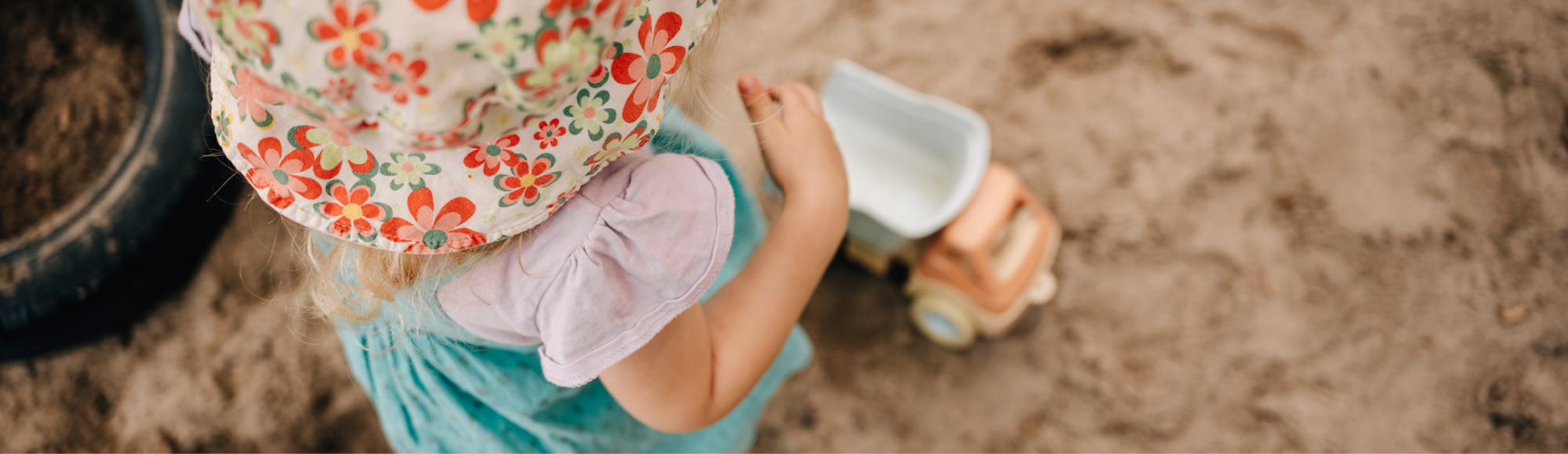 Kind steht im Sandbereich mit einem Spielzeugbagger